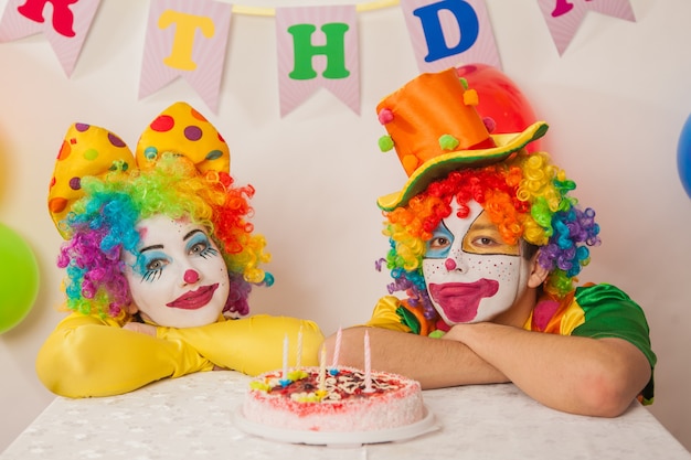 Pagliacci emotivi felici in vacanza cercando di mangiare la torta di compleanno