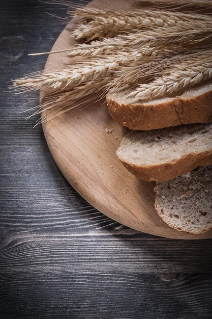 Pagnotta di pane affettata su tavola da intaglio in legno vista dall'alto di spighe di segale di grano dorato