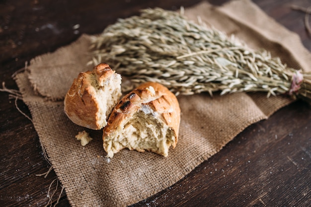 Pagnotta di pane appena sfornata con crosta croccante spezzata a metà e mazzo di grano su tela di juta. Concetto di panetteria artigianale, alimenti biologici naturali.