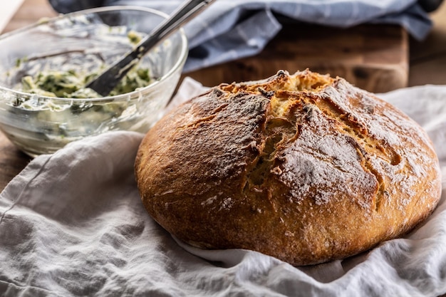 Pagnotta di pane appena sfornata su un asciugamano di lino accanto a una ciotola di burro alle erbe