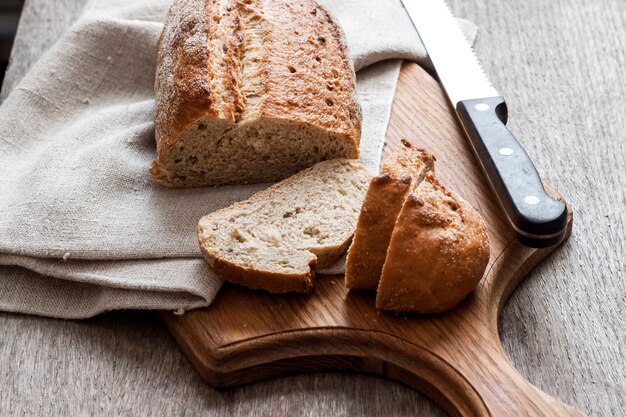 Pagnotta di pane integrale con le fette sul bordo di legno sul tavolo da cucina