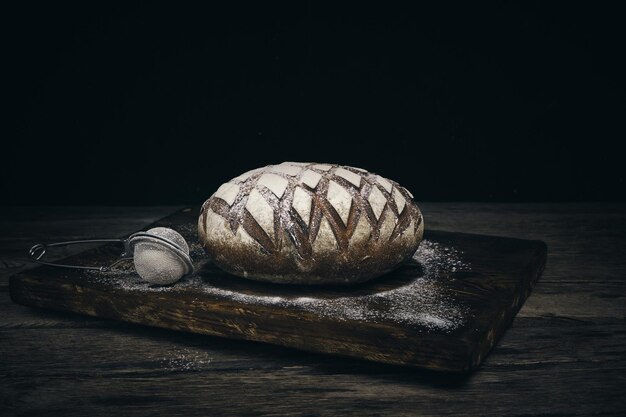 Pagnotta di pane nero di segale cosparso di farina e setaccio per cospargere su fondo scuro