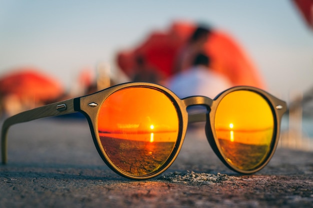Paio di occhiali da sole sulla spiaggia con il riflesso del tramonto