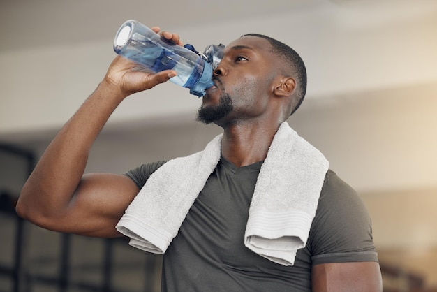 Palestra fitness e uomo di colore che beve acqua dopo l'allenamento o l'allenamento per l'idratazione, la salute o il benessere Forte atleta sano e africano che si gode una bevanda dopo un intenso esercizio fisico al centro sportivo