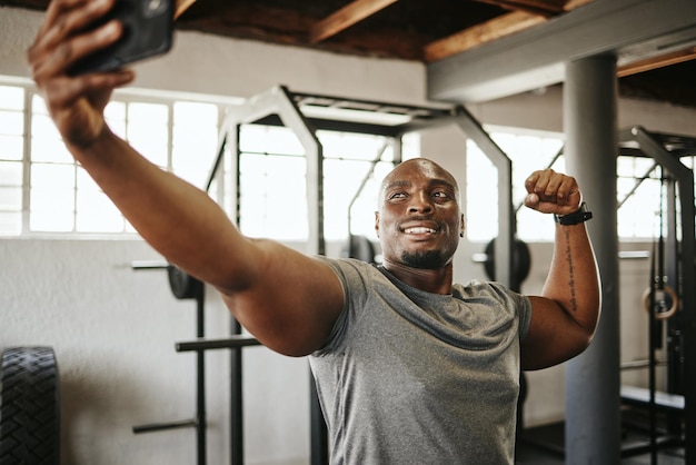 Palestra telefonica e selfie dell'esercizio e del fitness dell'uomo di colore con bodybuilder muscoloso e sorridente istruttore felice con foto motivata e pronta per un buon allenamento in un centro benessere