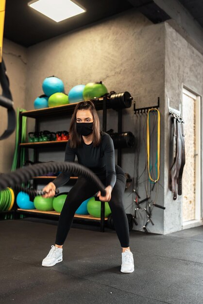 palestre al tempo del coronavirus. una donna con una maschera sul viso che si esercita con una corda in palestra.