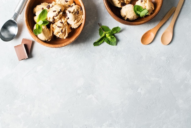 Paletta per gelato al caffè o al cioccolato in piatto di legno con foglia di menta su sfondo grigio chiaro