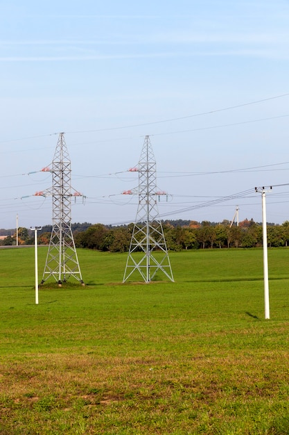 Pali elettrici e ad alta tensione in un campo con erba verde contro un cielo blu