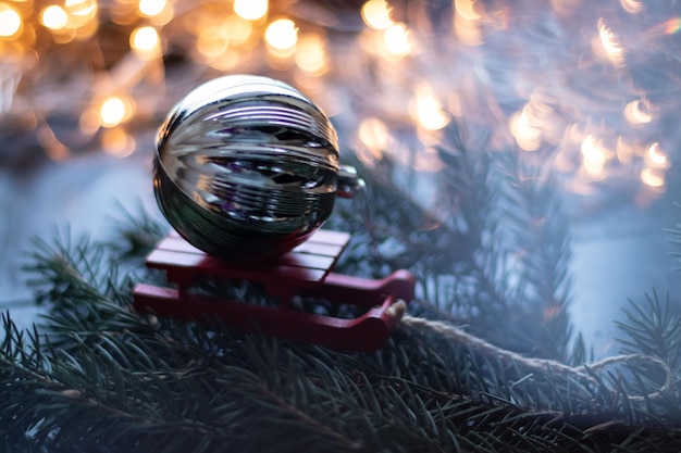 Palla d'argento di Natale su slitta rossa Ramo di albero di Natale con ghirlanda Effetto bokeh Foto premium