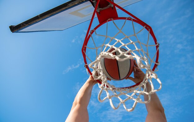 Palla da basket che vola attraverso il canestro nelle mani dei giocatori sul basket di sfondo del cielo