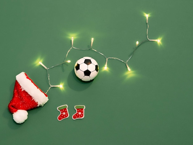 Palla da calcio a Natale Cappello di Babbo Natale su uno sfondo verde come un campo da calcio Natale nello sport