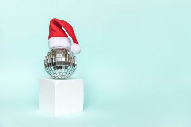 Palla da discoteca in cappello di Babbo Natale e forme di cubo forma geometrica podio isolato sfondo blu