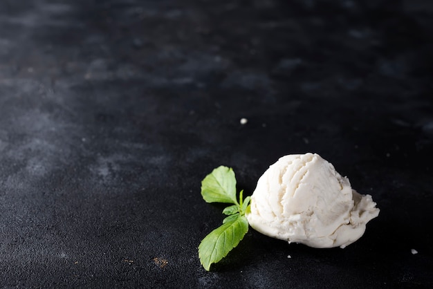 Palla di gelato alla vaniglia con foglie verdi su scuro