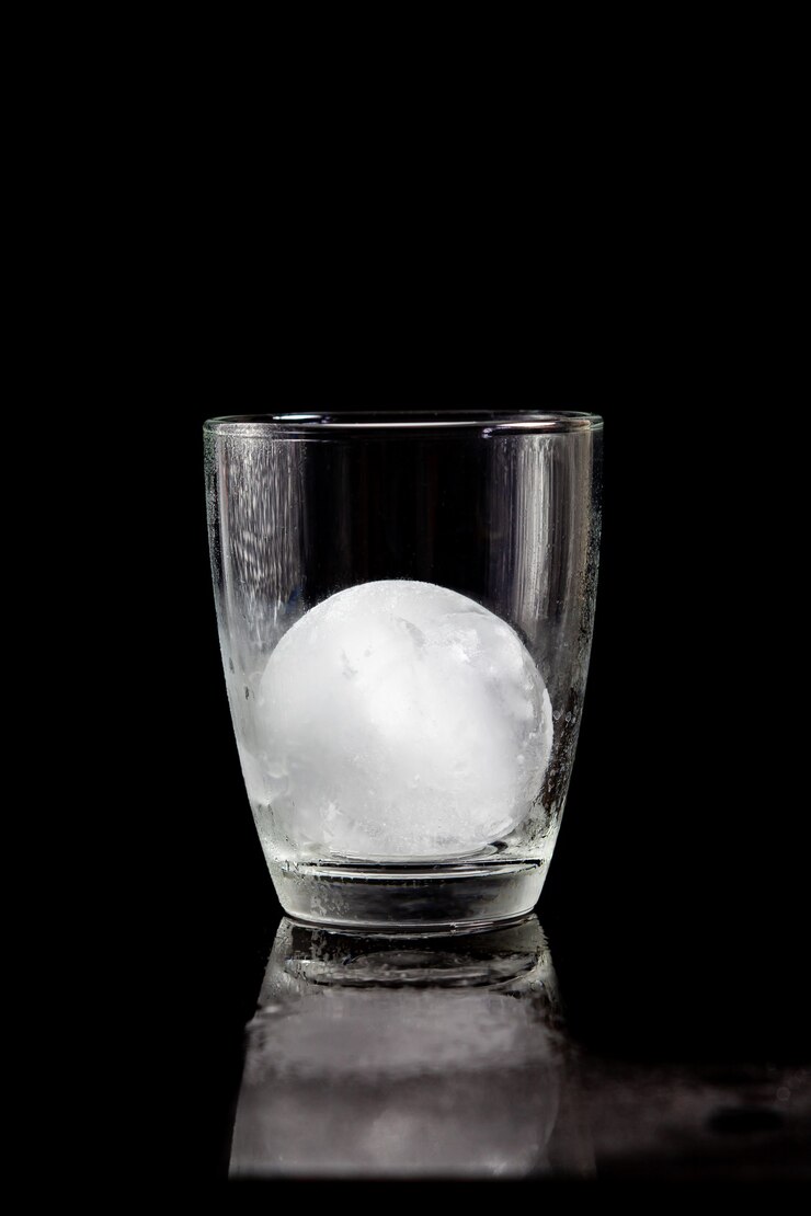 Palla di ghiaccio all'interno del bicchiere da cocktail su un tavolo nero riflettente.