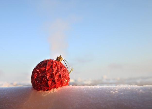 Palla di Natale rossa nella neve su uno sfondo di cielo sfocato. Palla di vetro di Natale.