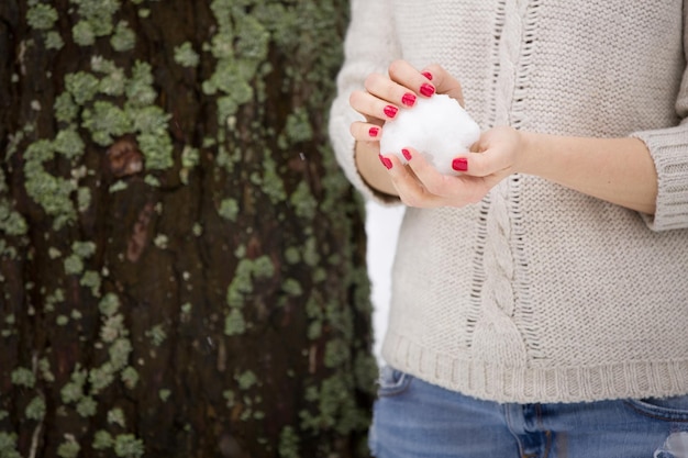 Palla di neve nelle mani di una giovane donna con manicure rossa e maglione caldo L'inverno cammina all'aperto