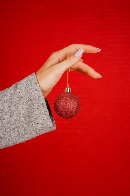 Palla rossa rotonda dell'albero di Natale in mano femminile isolata su sfondo rosso la mano di una donna tiene a