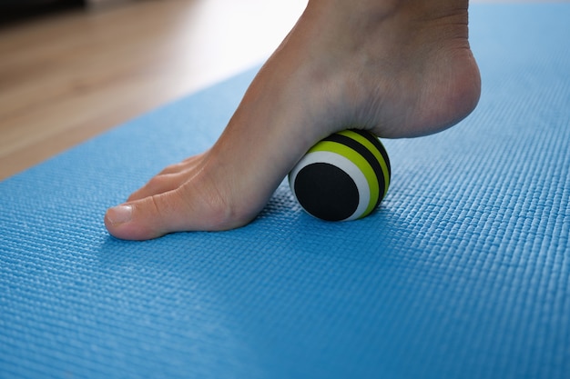 Palla sportiva che rotola la gamba della donna per la prevenzione e il trattamento del primo piano dei piedi piatti