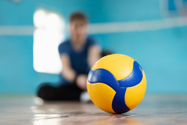 Pallavolo con una ragazza sportiva sullo sfondo che si prepara per l'allenamento Giocando a pallavolo concetto nuova palla sul pavimento sul campo