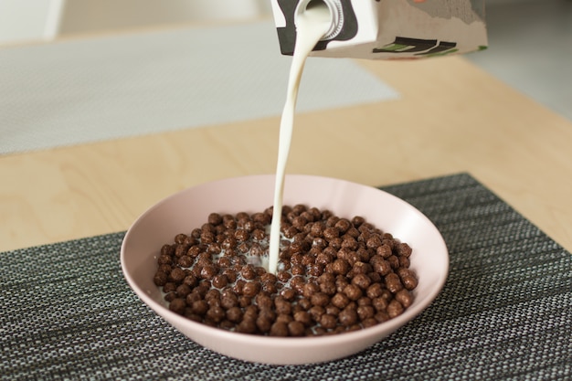 Palle di cereali al cioccolato con latte in una ciotola sul tovagliolo sul tavolo di legno.