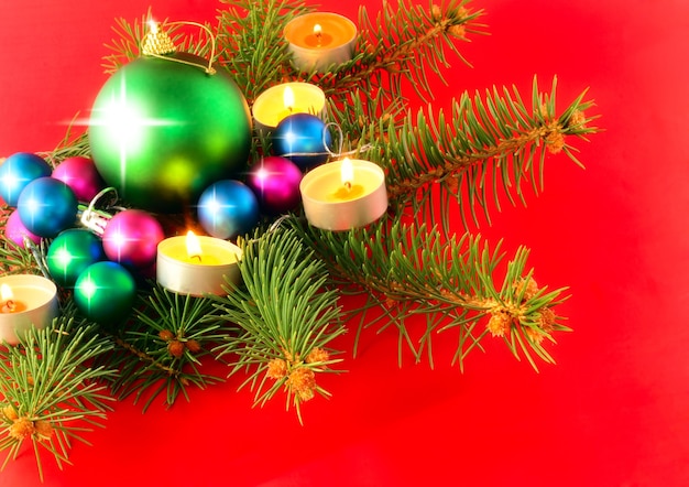 Palle di decorazione di Natale e Capodanno con rami di abete e candele su sfondo rosso.