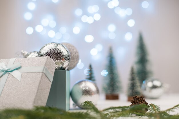 Palle di Natale d'argento in una confezione regalo su uno sfondo di alberi di Natale e bokeh blu.