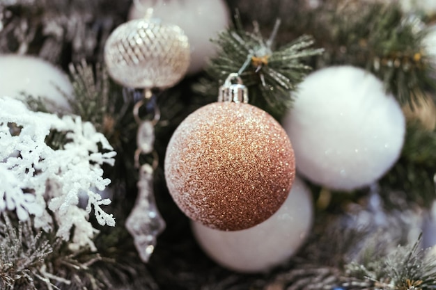 Palle di Natale in oro e bianco con scintillii su un primo piano innevato dell'albero di Natale