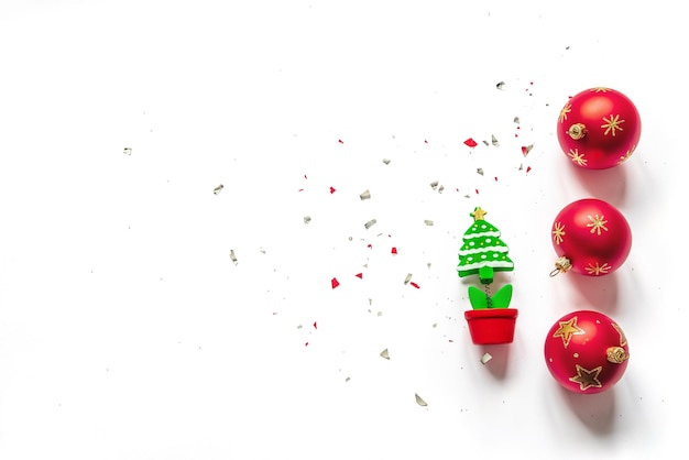 Palle di Natale rosse, un modello di abete in miniatura e coriandoli su sfondo bianco