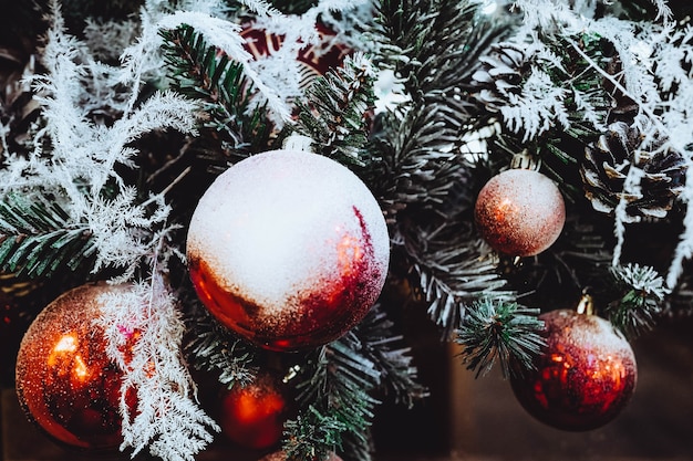 Palle rosse di Natale appese ai rami di un albero di Natale ricoperto di neve bianca. Decorazione festiva all'interno.