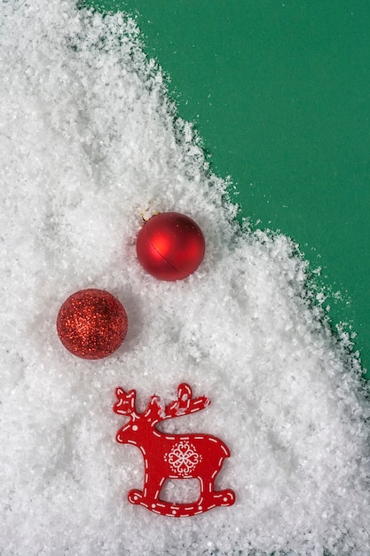 Palle rosse di Natale e figurina di un cervo nella neve su uno sfondo verde con spazio per le copie. Vista dall'alto.