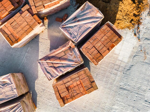 Pallet con mattoni in ceramica rossa sul tetto di un edificio in costruzione Lavori preparatori per la posa dei mattoni Vista dall'alto del cantiere