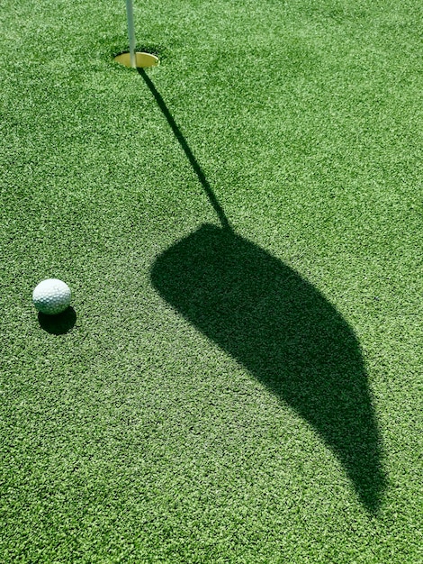 Pallina da golf sul green, ombra di una bandiera su un green, campo da golf