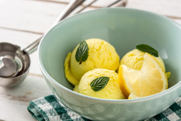 Pallina di gelato al limone decorata con foglie di menta sul tavolo di legno bianco