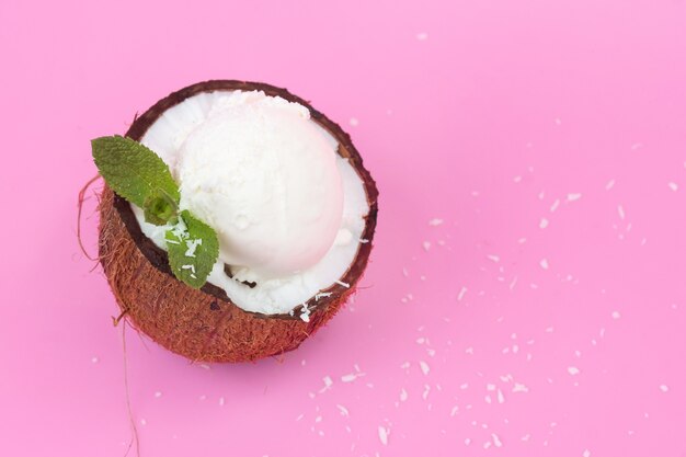 Pallina di gelato alla vaniglia in cocco fresco per metà decorata con foglie di menta su fondo rosa