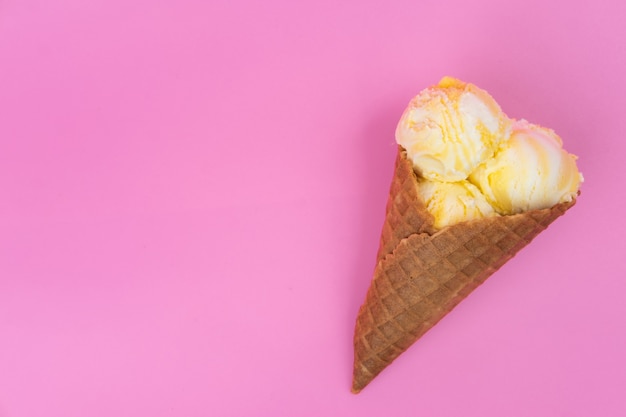 Palline di gelato al profumo di frutta in un cono di cialda su sfondo rosa.