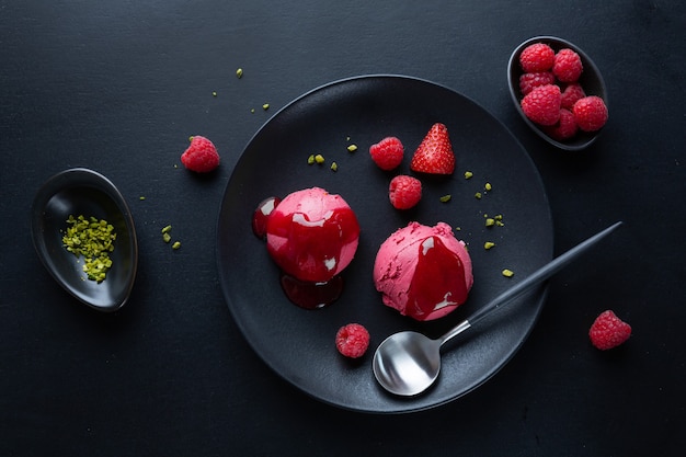 Palline di gelato alla fragola alla frutta con salsa di fragole servite su piatto con frutta e pistacchi. Vista dall'alto.