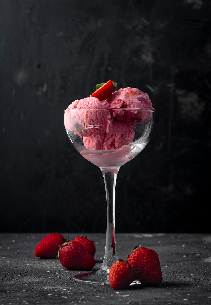 Foto palline di gelato alla fragola con bacche di fragola, in un bicchiere alto trasparente su uno sfondo scuro