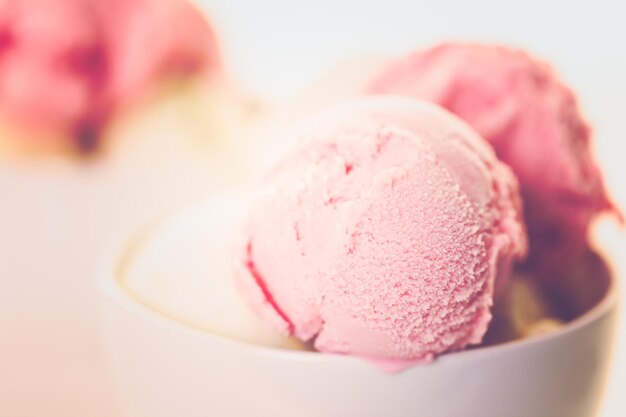 Palline di gelato alla vaniglia e fragola in una tazza bianca.