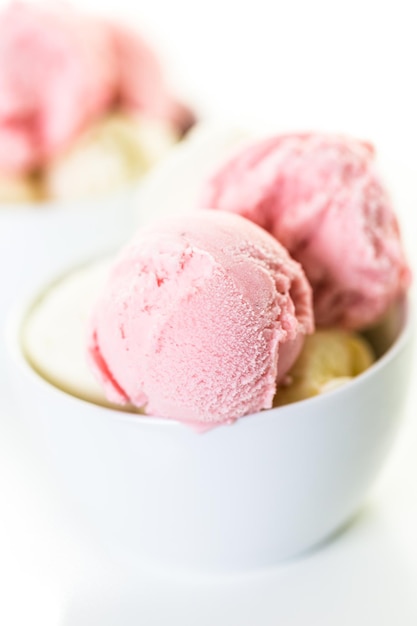 Palline di gelato alla vaniglia e fragola in una tazza bianca.