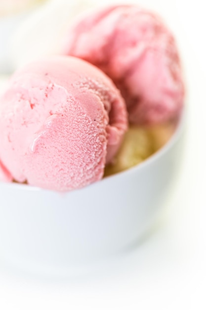 Palline di gelato alla vaniglia e fragola in una tazza bianca.