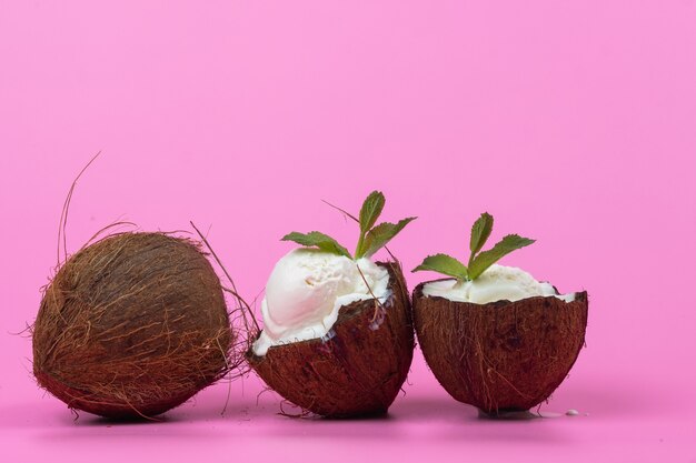 Palline di gelato alla vaniglia in metà di cocco fresco decorate con foglie di menta su sfondo rosa.