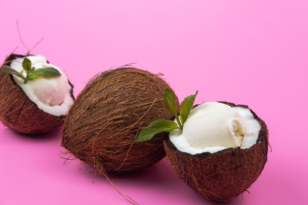 Palline di gelato alla vaniglia in metà di cocco fresco decorate con foglie di menta su sfondo rosa.