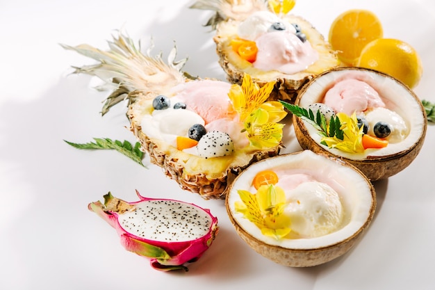 Palline di gelato decorazione fiori e frutti di bosco a metà di cocco e ananas. Concetto tropicale estivo.