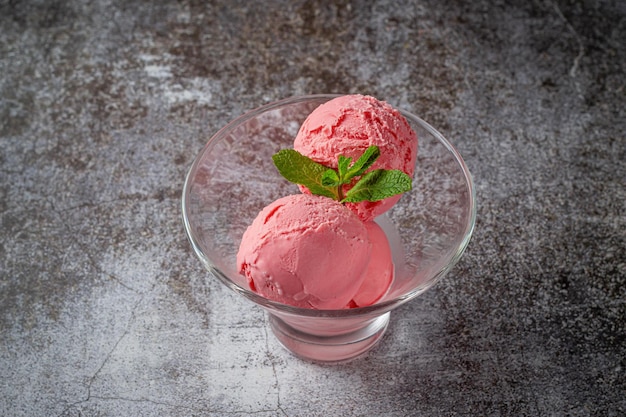 Palline rosa di gelato alla fragola in un bicchiere di vetro su una pietra grigia