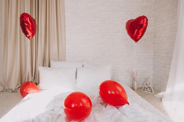 Palloncini a cuore rosso in una camera da letto con un letto bianco. San Valentino