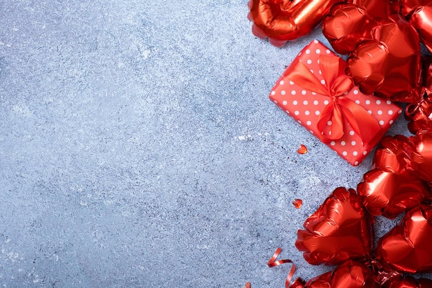 Palloncini a forma di cuore rosso e confezione regalo su sfondo concreto Modello di biglietto di auguri di San Valentino Copia spazio