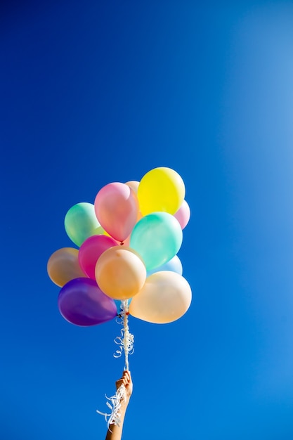 Palloncini colorati tenuti in mano contro il cielo blu