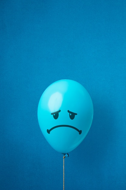 Palloncino blu con una faccia triste disegnata. Concetto di lunedì blu