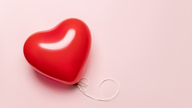 Palloncino rosso a forma di cuore su sfondo rosa pallido. San Valentino concetto.