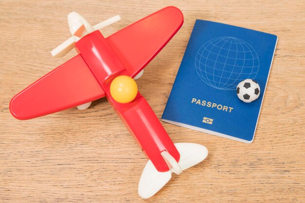 pallone da calcio in miniatura su un aereo giocattolo e passaporto sdraiato su un tavolo di legno su una mappa di sfondo